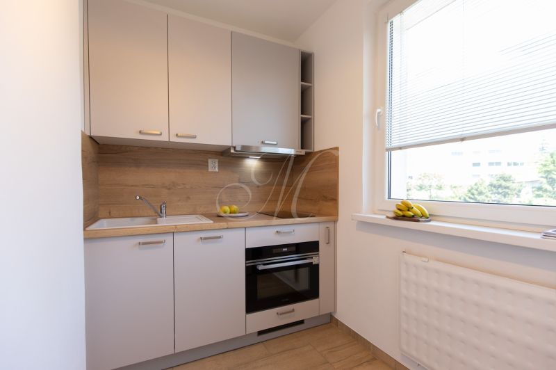 A kitchen in a 2-room apartment with wooden decor and fruit by the window.
