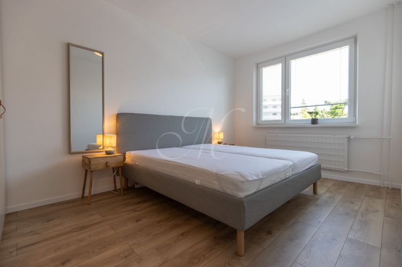 A bedroom in a two-room apartment with a wooden decor floor, a gray bed, and a nightstand.