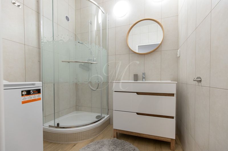 A bathroom in a 2-room apartment with a round mirror, a shower corner, and a floor with a wooden decor.