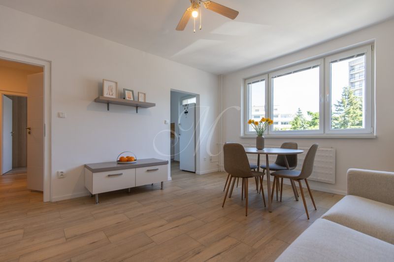 Living room in a two-room apartment with a wooden decor floor and a dining table.