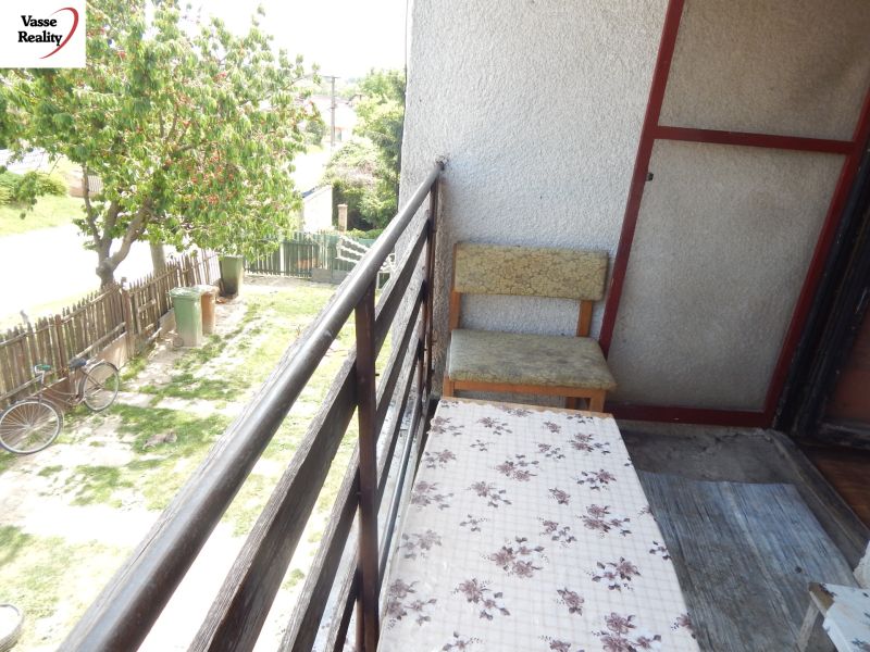 The balcony of a family house in Strekov with seating, a view of the yard, and a tree.