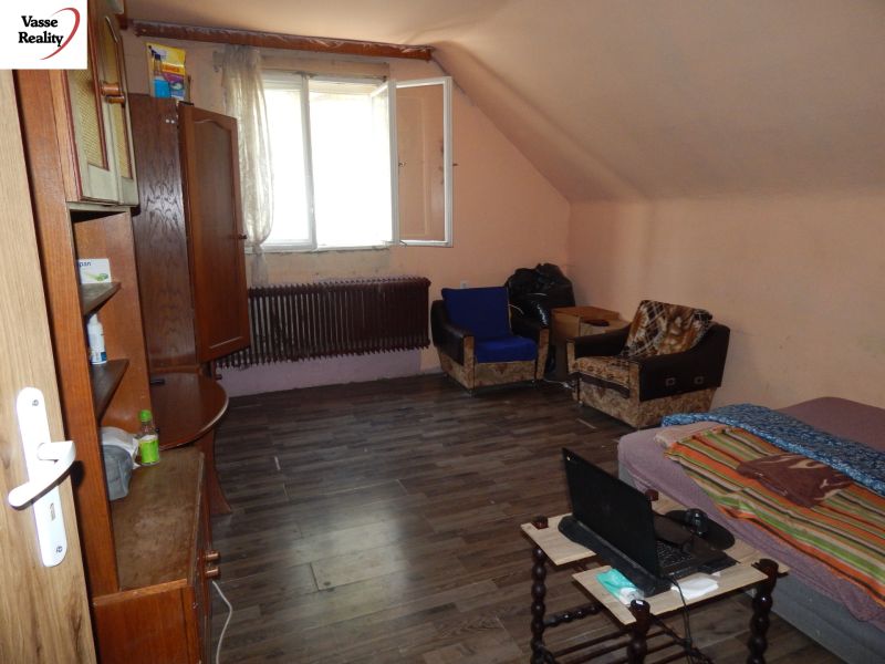 A room in a family house with a wooden decor floor, simple furnishings, and an open window.