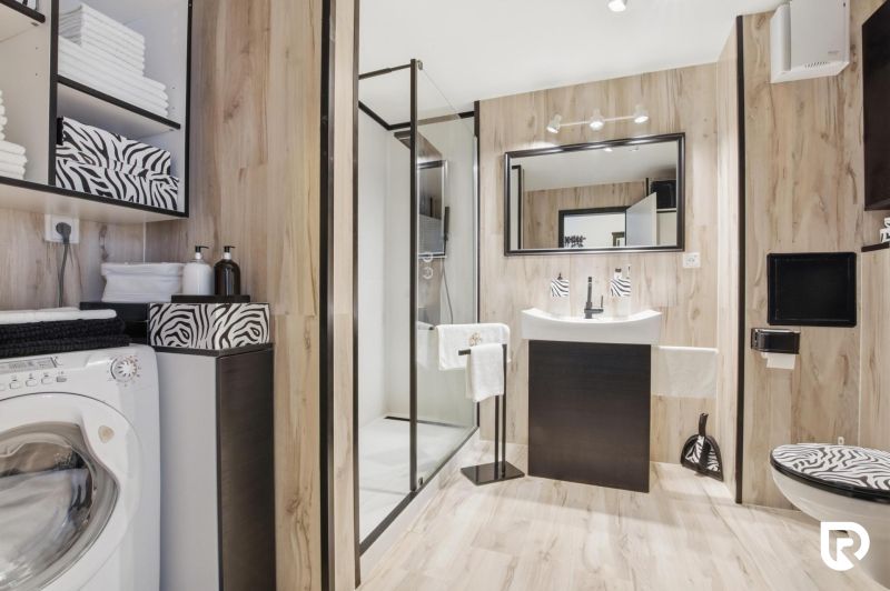 Bathroom in a 2-room apartment with a washing machine, shower, and floor with wood decor.