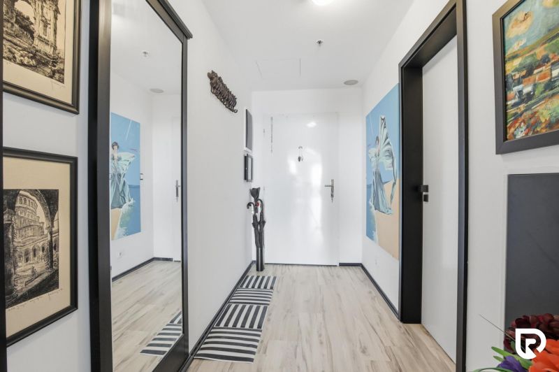 The entrance hall of a 2-room apartment with a wooden decor floor, a mirror, and art on the walls.