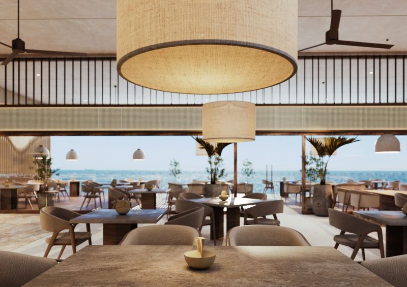 A restaurant with an ocean view, comfortable seating, large hanging lights.