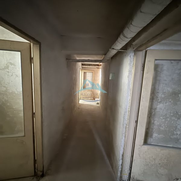 A narrow corridor with doors in commercial premises, plastered walls, older equipment.