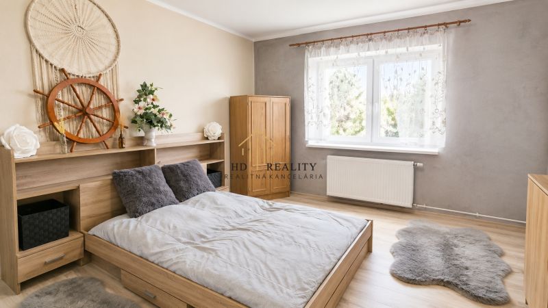 Bright bedroom in a family house with a bed, decorations, and a wooden-patterned floor.