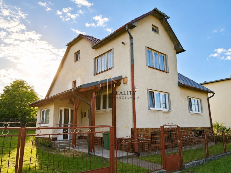 A family house in Sebechleby with a fence and a landscaped garden under a blue sky.