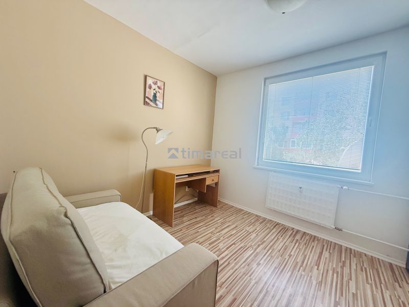 A room in a 3-room apartment with a sofa, a table, a wooden decor floor, and a large window.