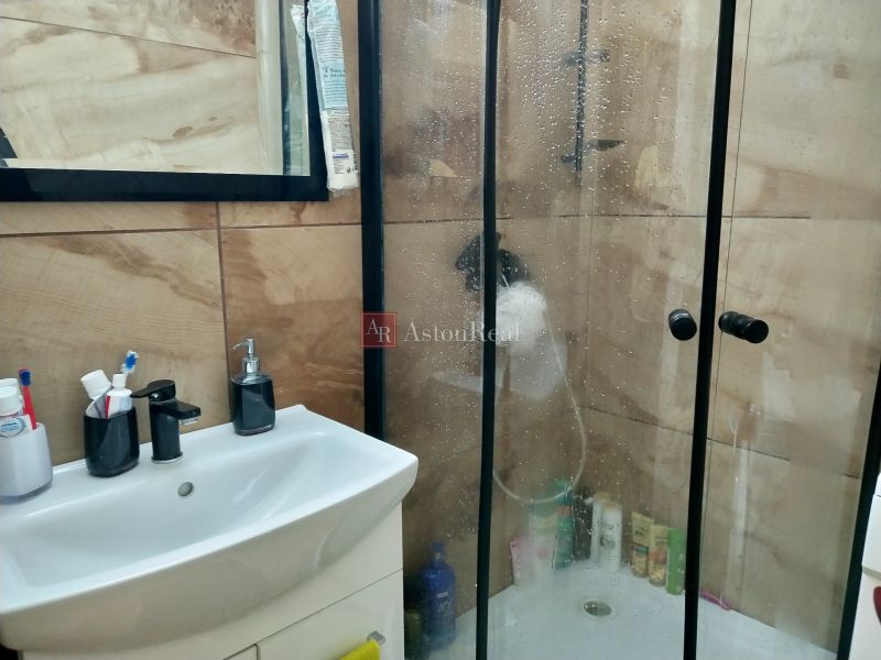 Bathroom in a 2-room apartment with a shower and a sink, tiled with wood decor.