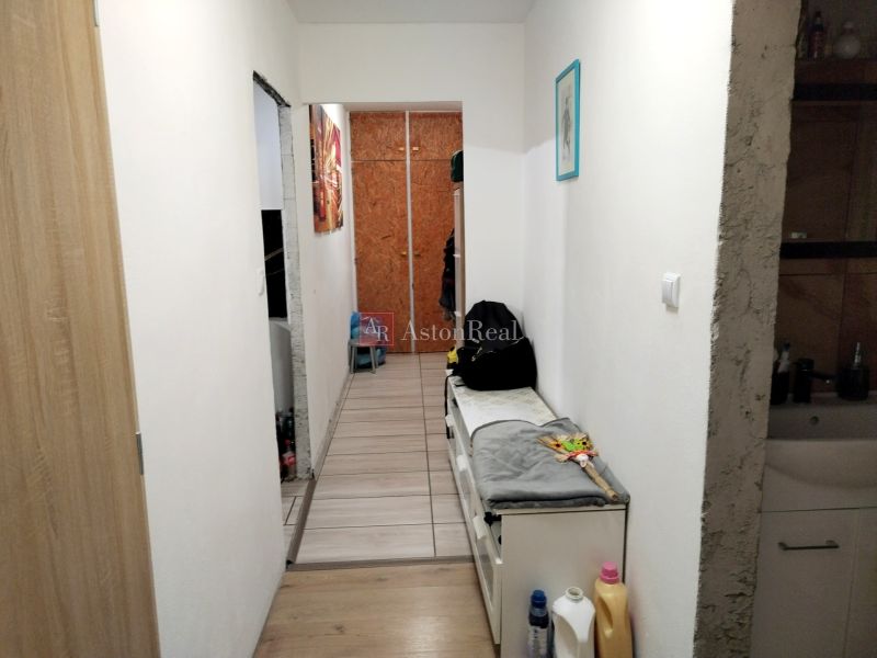 A narrow hallway in a 2-room apartment with a wooden decor floor and white walls.