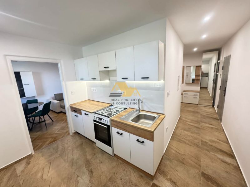 A kitchen in a 2-room apartment with tiles and a wooden decor on the cabinets.