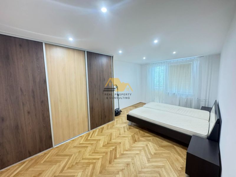 A bedroom with a wood-patterned floor and a large built-in wardrobe in a 2-room apartment.