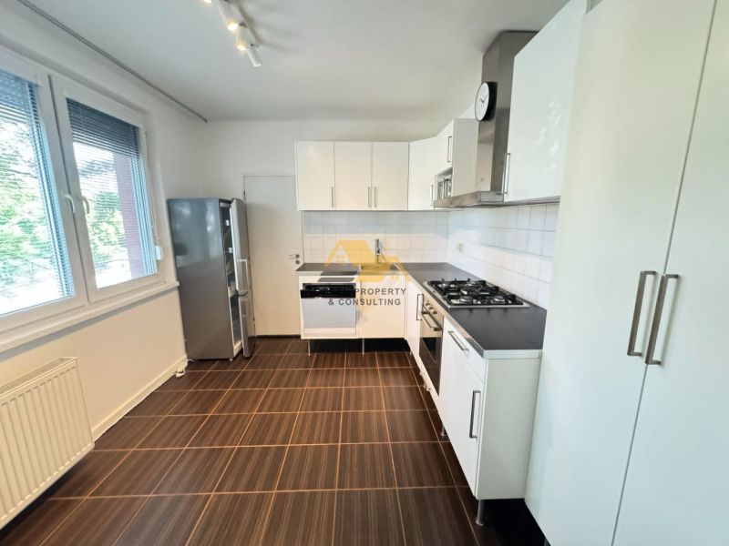 A kitchen in a 3-room apartment with white cabinets, a stove, and large windows, with a wooden decor floor.
