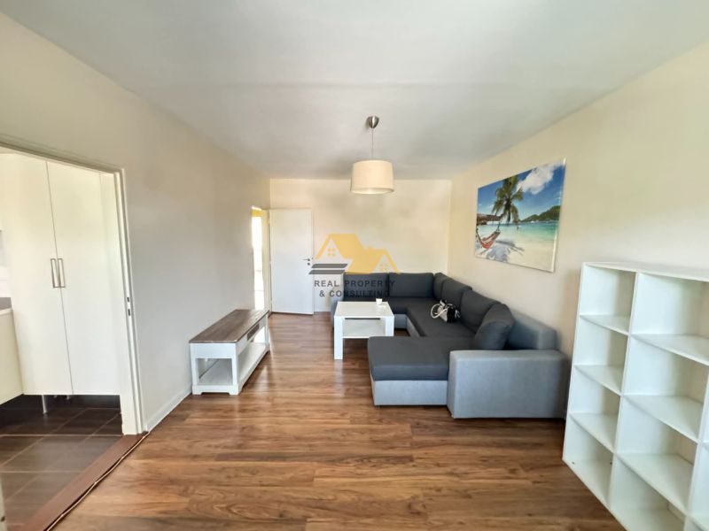 A living room with a wood-patterned floor and a comfortable gray sofa in a three-room apartment.