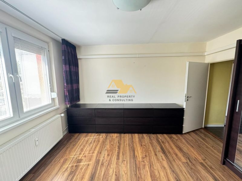 A bedroom in a 3-room apartment with a wood-patterned floor and a large dresser.