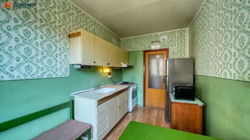 Kitchen of a 4-room apartment with wallpaper, wood-patterned flooring, and basic equipment.