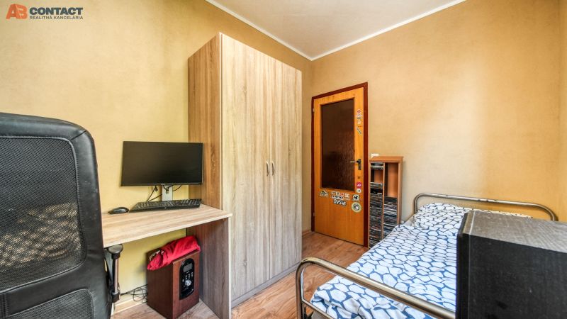 A room with a table, monitor, wardrobe, and bed, in a 4-room apartment, with a wooden decor floor.