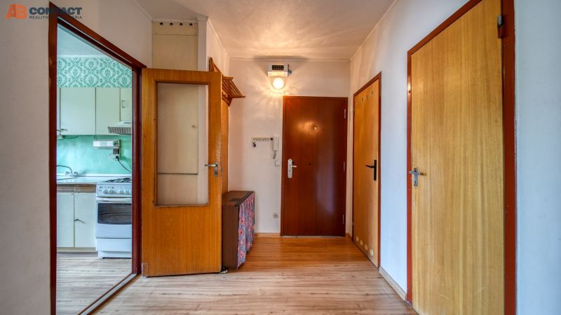 A hallway in a 4-room apartment with a wooden decor floor and a view of the kitchen.
