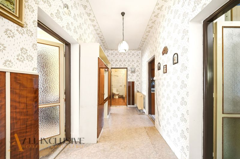 A hallway in a family house with patterned wallpaper, a display cabinet, and a door to the bathroom.
