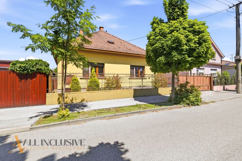A family house in Dunajská Streda with a front garden, fencing, and trees along the road.