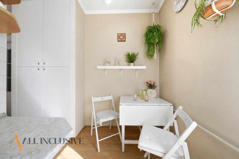 Dining area of a 3-room apartment with plants and white furniture, floor with wooden decor.