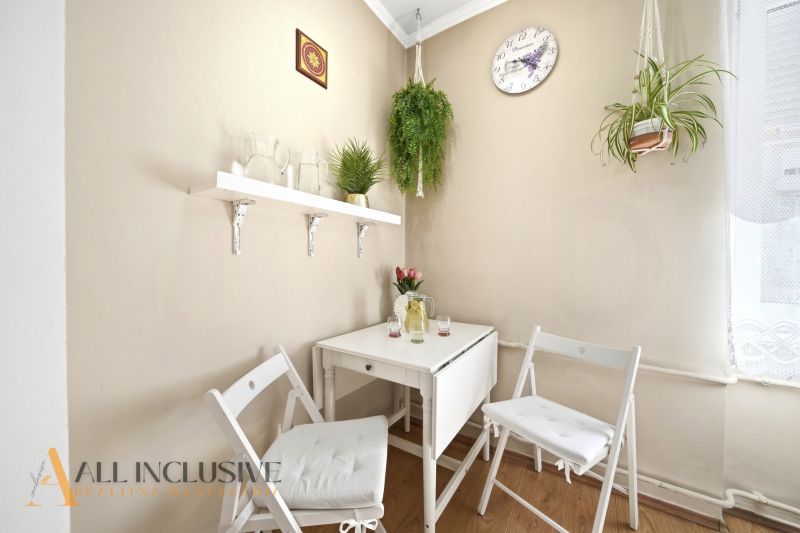 Kitchen corner in a 3-room apartment with a white table, hanging plants, and a wooden decor floor.