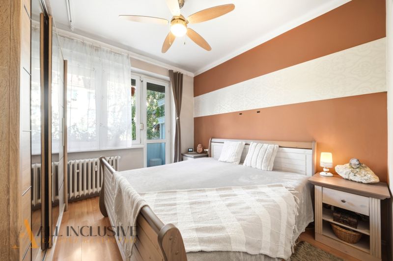 A bedroom in a 3-room apartment with a wood-patterned floor, a fan, and balcony windows.