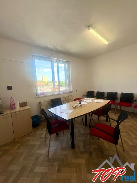 An office with a wooden floor, a desk, chairs, and a window in a commercial space.
