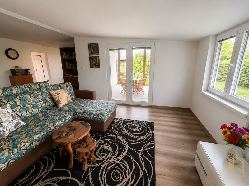 Living room in a cottage with a floral sofa, tables, and a view of the garden.