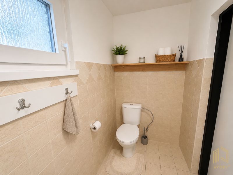 A bathroom in a cabin with beige tiles and a wooden shelf above the toilet.