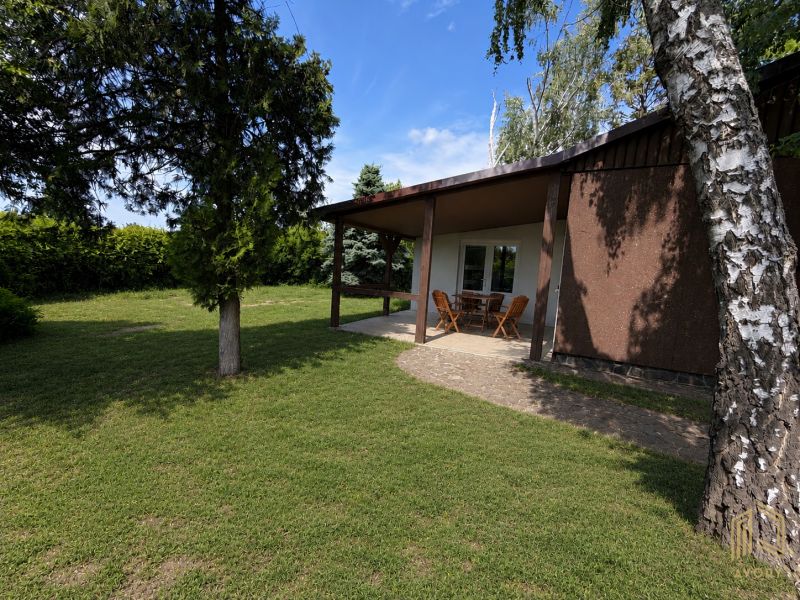 A cottage in Kopčany with a garden, terrace, and wooden furniture against a backdrop of greenery.