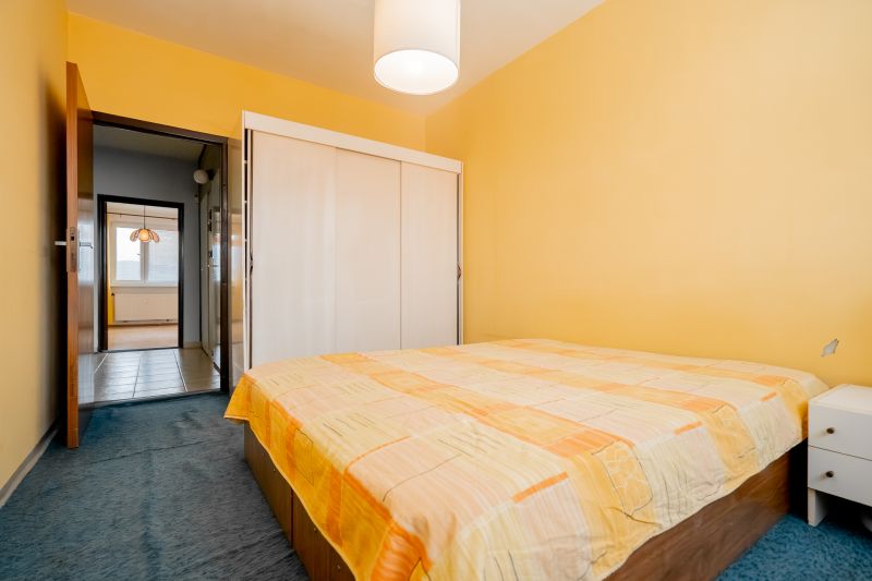 Bedroom with orange walls and a bed in a 3-room apartment, passage to the hallway.