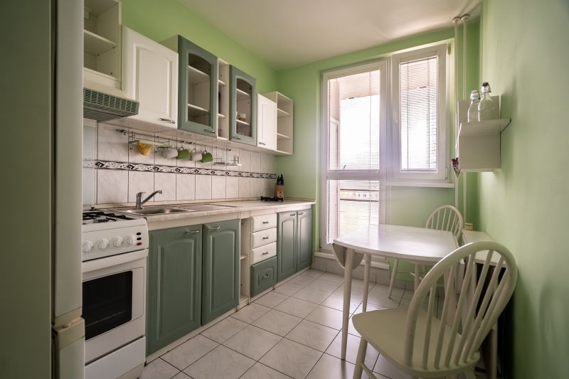 A kitchen in a 3-room apartment with white appliances, a green wall, and a dining table.