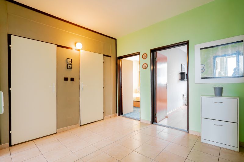 A hallway in a 3-room apartment with a ceramic floor, green wall, and bright lighting.