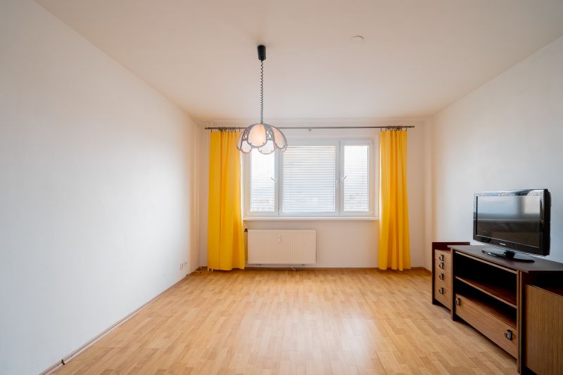Living room in a 3-room apartment with a wooden decor floor and yellow curtains.