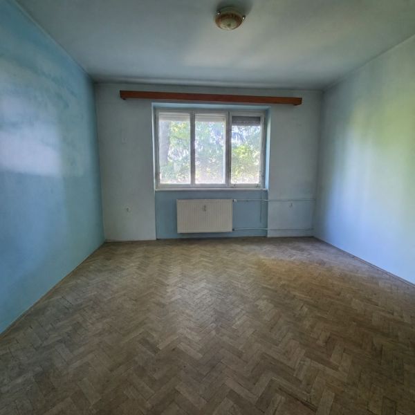An empty room with a wooden floor and blue walls in a 3-room apartment.
