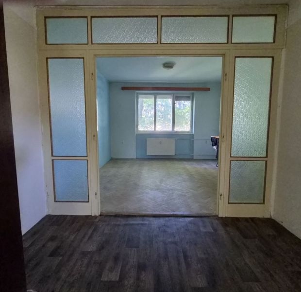 A living room in a three-room apartment with a wooden decor floor and glass doors.