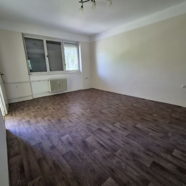 A room in a 3-room apartment with a wooden decor floor and a large window.