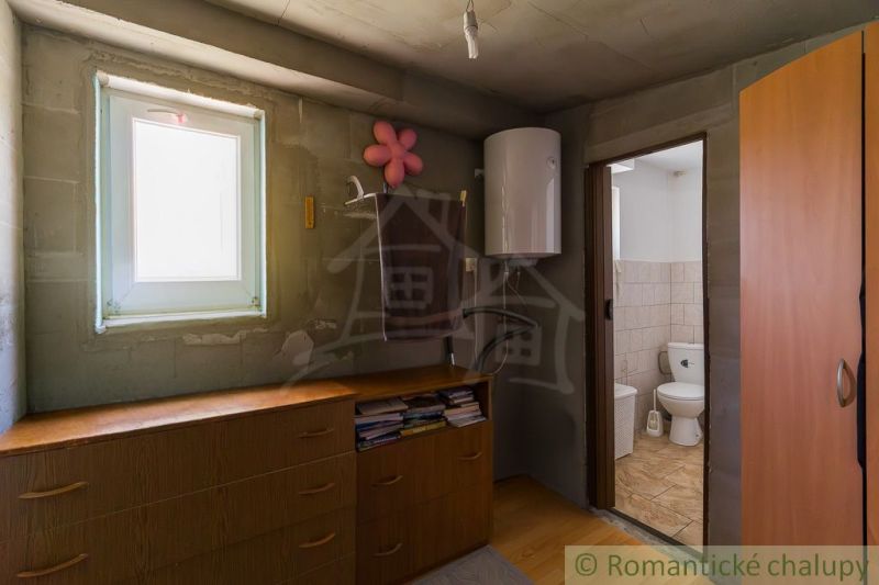 A cabin with a wooden decor floor, a dresser, a boiler, and an entrance to the bathroom.