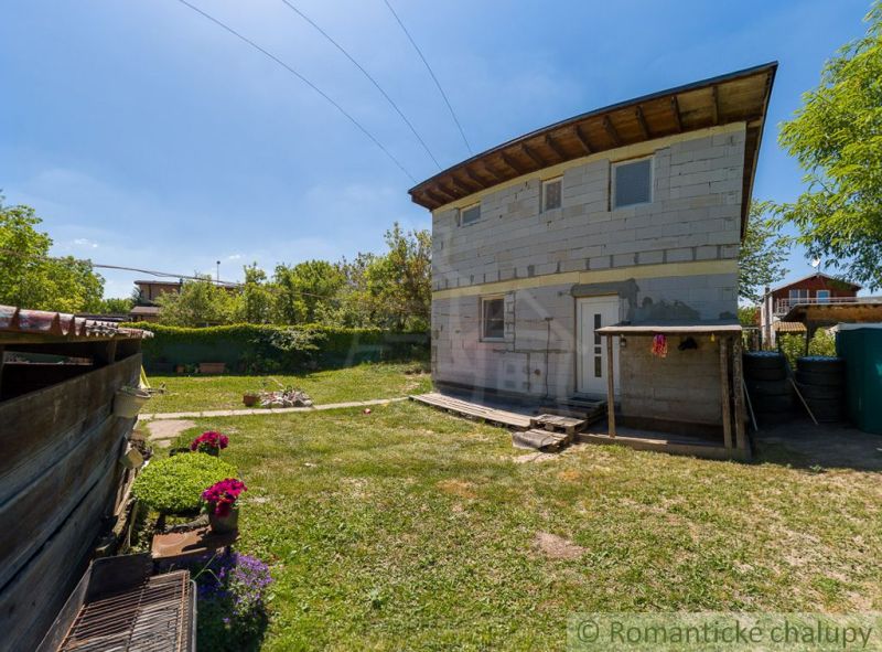 A cottage in Bernolákovo with an uninsulated facade, a lawn, and ornamental plants in the garden.