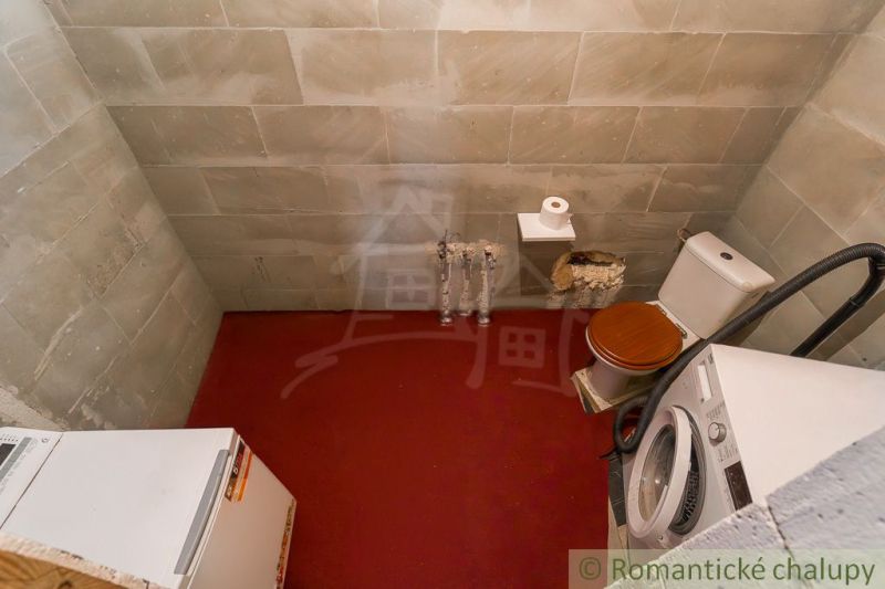 A bathroom in a cabin with older equipment, a washing machine, and a toilet.