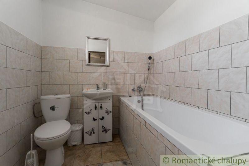 A bathroom in a cottage with a bathtub, sink, and toilet, with tiles on the walls.