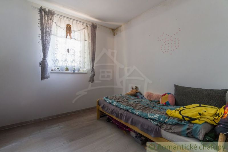 A room in a cottage with a bed and flowers on the windowsill, a floor with a wooden decor.