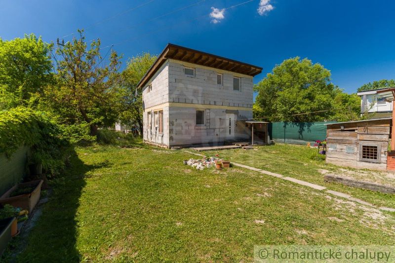A cottage in Bernolákovo surrounded by green trees, with a spacious lawn and blue sky.