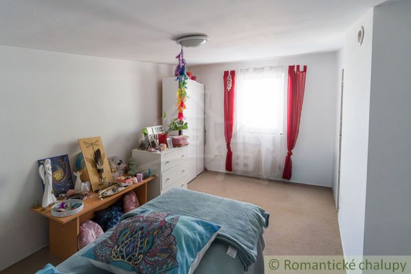 A bedroom in a cottage with white furniture, decorations, and red curtains.