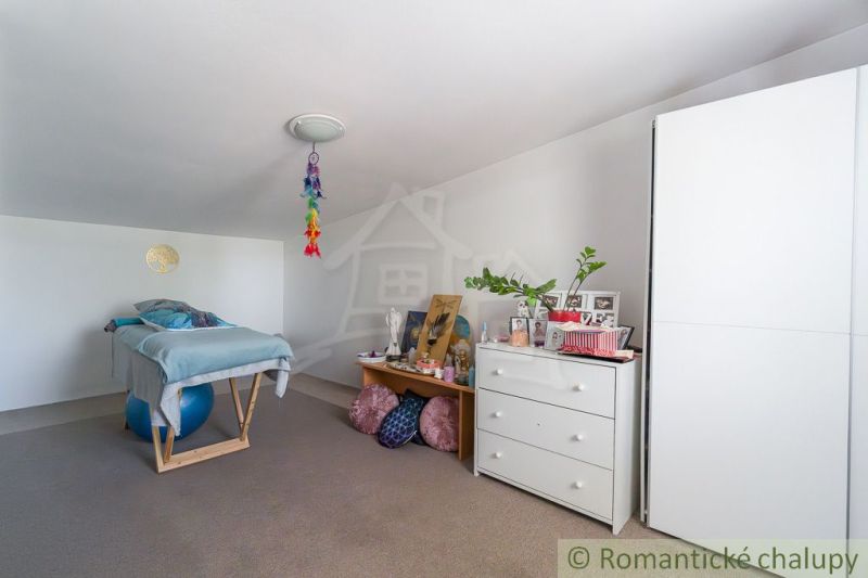 Interior of a cabin with a sloped ceiling, a bed on a ball, and decorations on the dresser.