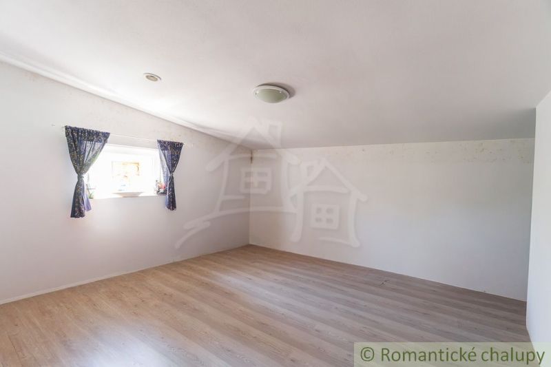 A spacious room in a cottage with a wooden decor floor and a window with blue curtains.