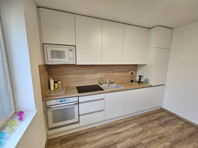 A kitchen with white cabinets, appliances, and a wood-patterned floor in a studio apartment.