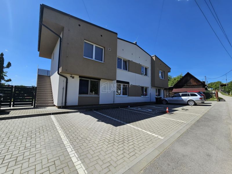 Apartment building in Štiavnik, Štiavnik with a parking lot and sunny sky suitable for a 1-bedroom apartment.